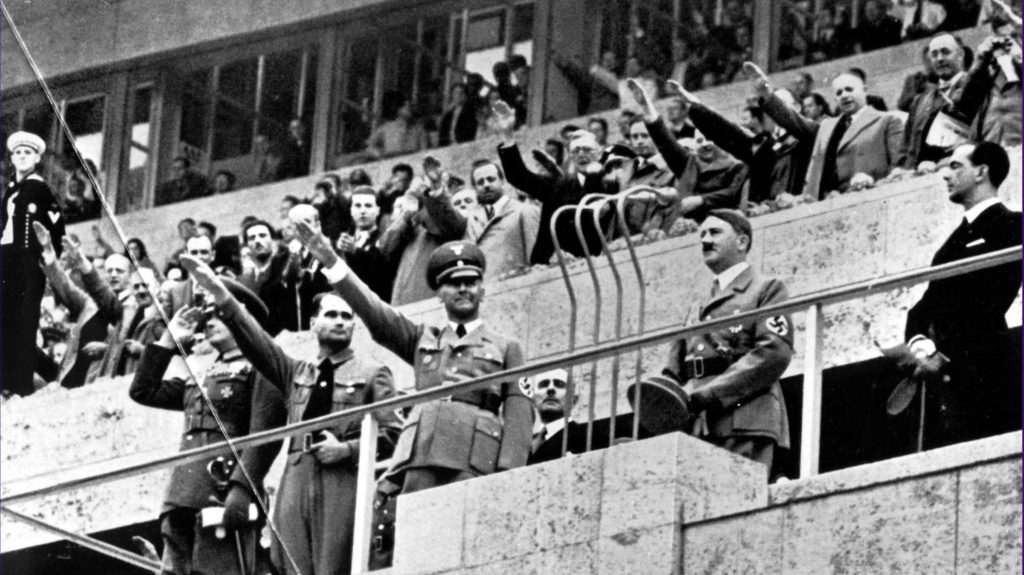 一张黑白照片，一群身着军装和正装的男子站在阳台上，向下面的人群敬礼。