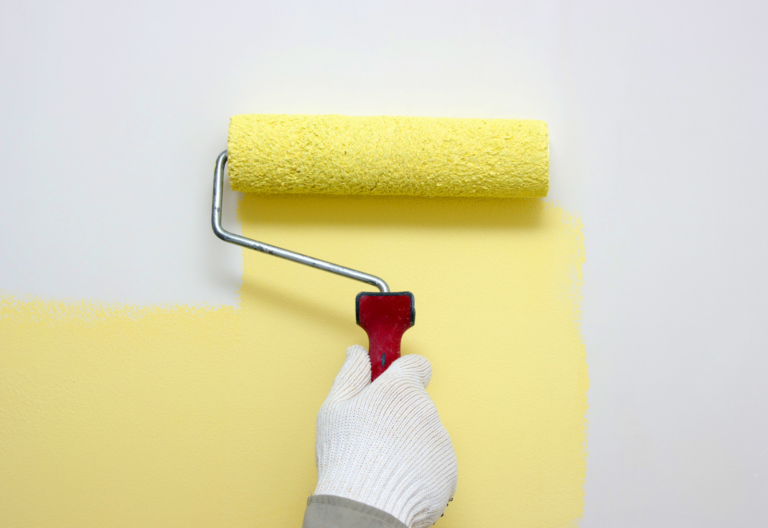 persona con guante blanco pintando una pared blanca con pintura amarilla