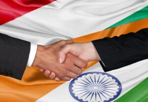 Two people in business attire shaking hands over a background of the indian flag.