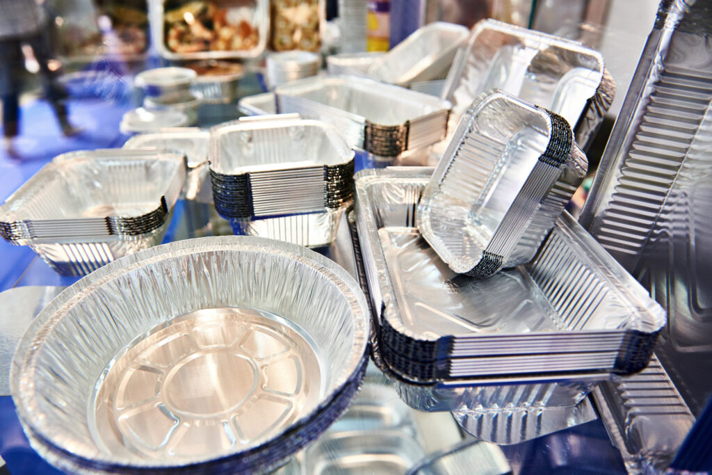 A variety of aluminum food containers, including round and rectangular shapes, are displayed on a reflective surface.