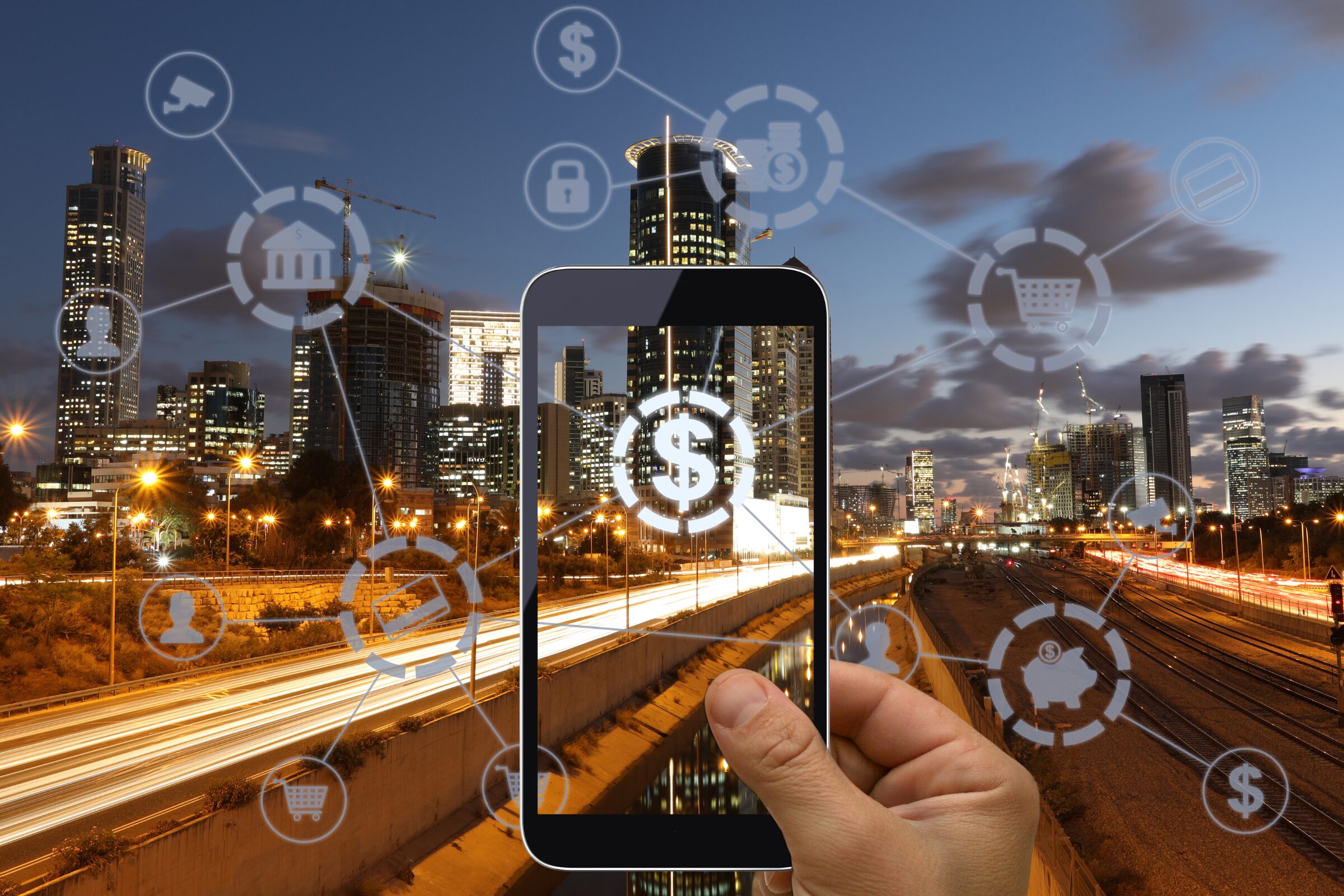 A hand holds a smartphone with connected icons of money, shopping, and banking overlaid on a cityscape at dusk, illustrating digital connectivity in a financial technology context.