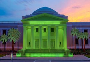 The supreme court building of Florida illuminated in green light against a twilight sky.