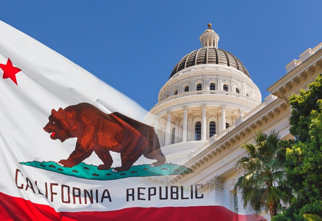Bandera del estado de california con un oso pardo delante del edificio del capitolio del estado de california con un cielo azul despejado.