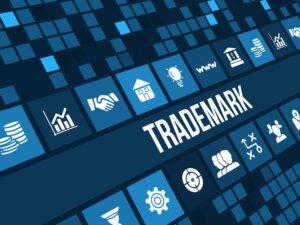 A digital graphic with the word "TRADEMARK" in the center, surrounded by various blue and white icons representing business and technology concepts.