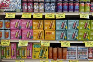 Shelves in a store display various cannabis-infused beverages and products, each labeled with price tags indicating discounts.