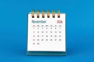 A desk calendar shows the month of November 2026 with dates arranged in a grid, set against a plain blue background—marking a year since the hemp bill November 2025 shaped new hemp compliance for 2026.