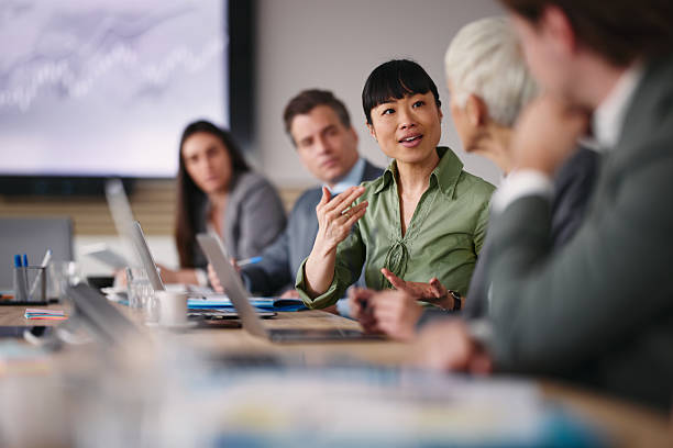 A group of professionals sit at a conference table with laptops, engaging in a discussion during a business meeting.