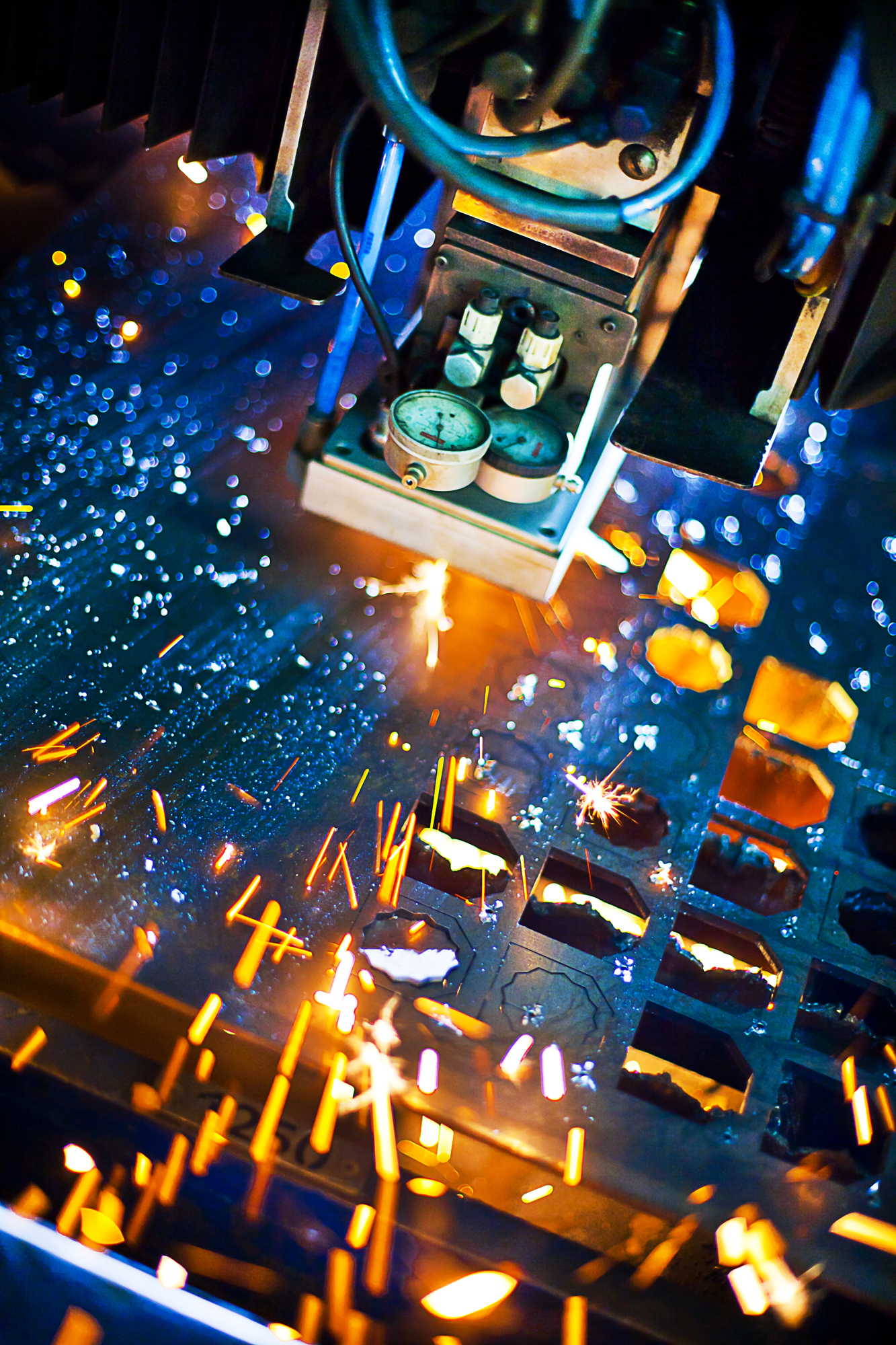 Close-up of a laser cutting machine processing a sheet of metal, emitting sparks and glowing embers during the cutting operation.