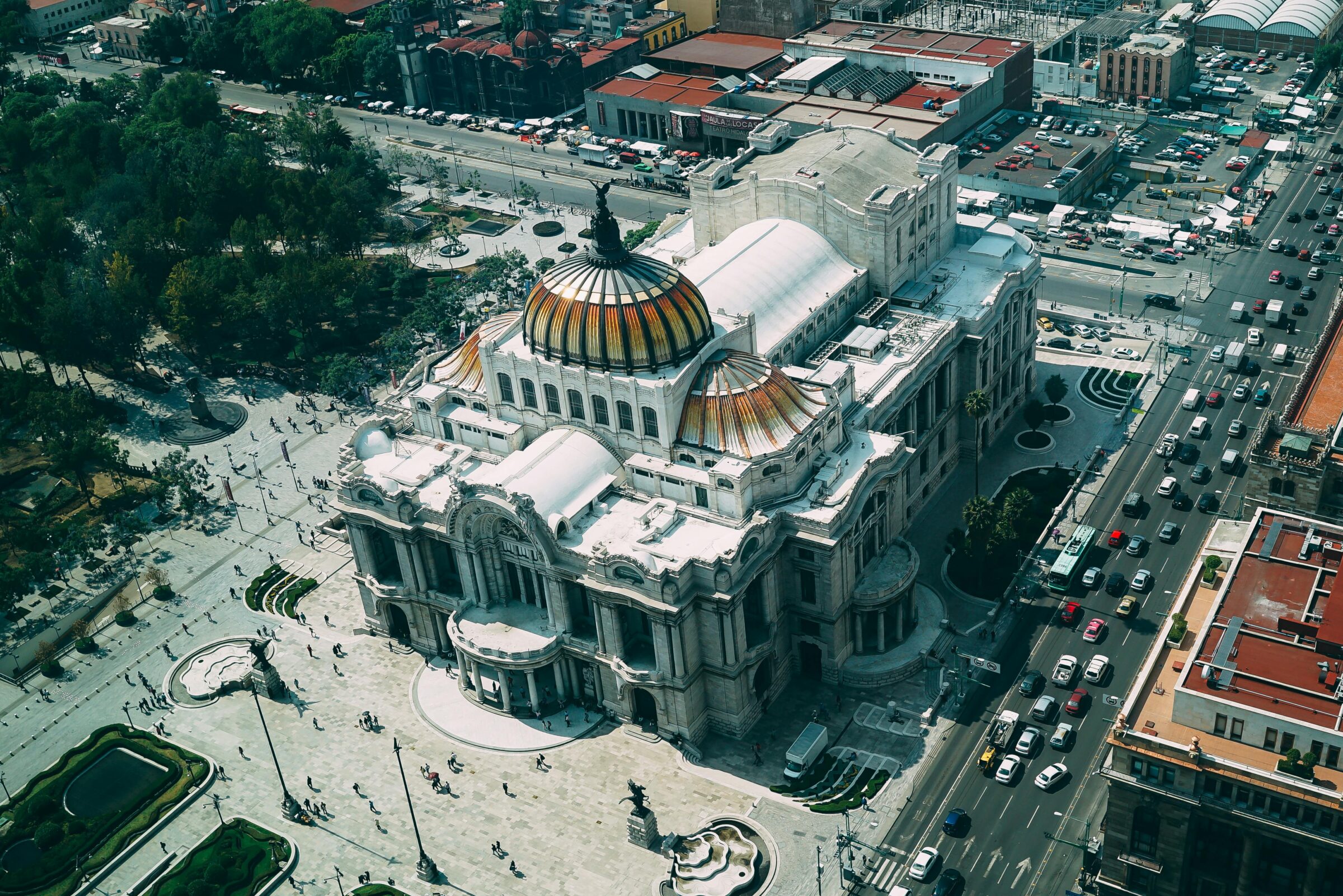 Aerial view of Palacio de Bellas Artes, a large, ornate building with a domed roof in Mexico City, surrounded by streets and greenery.